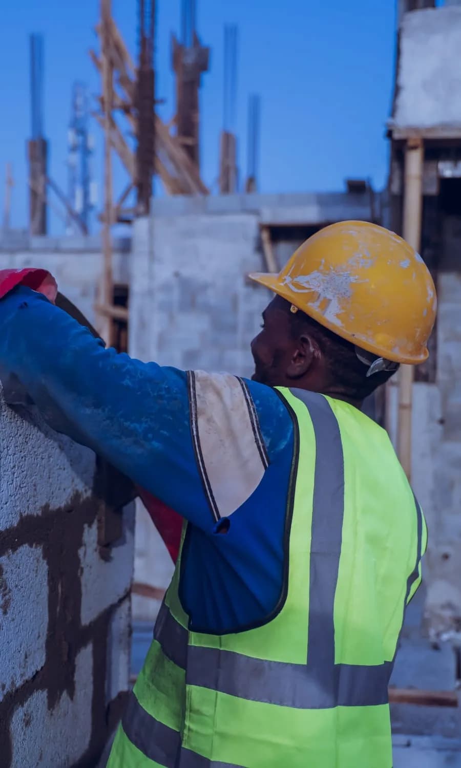 Maçon casqué posant un bloc de béton sur un mur
